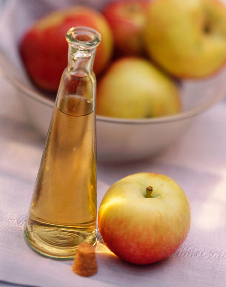 Apfelessig in einer Flasche neben Apfel; Äpfel in Schale