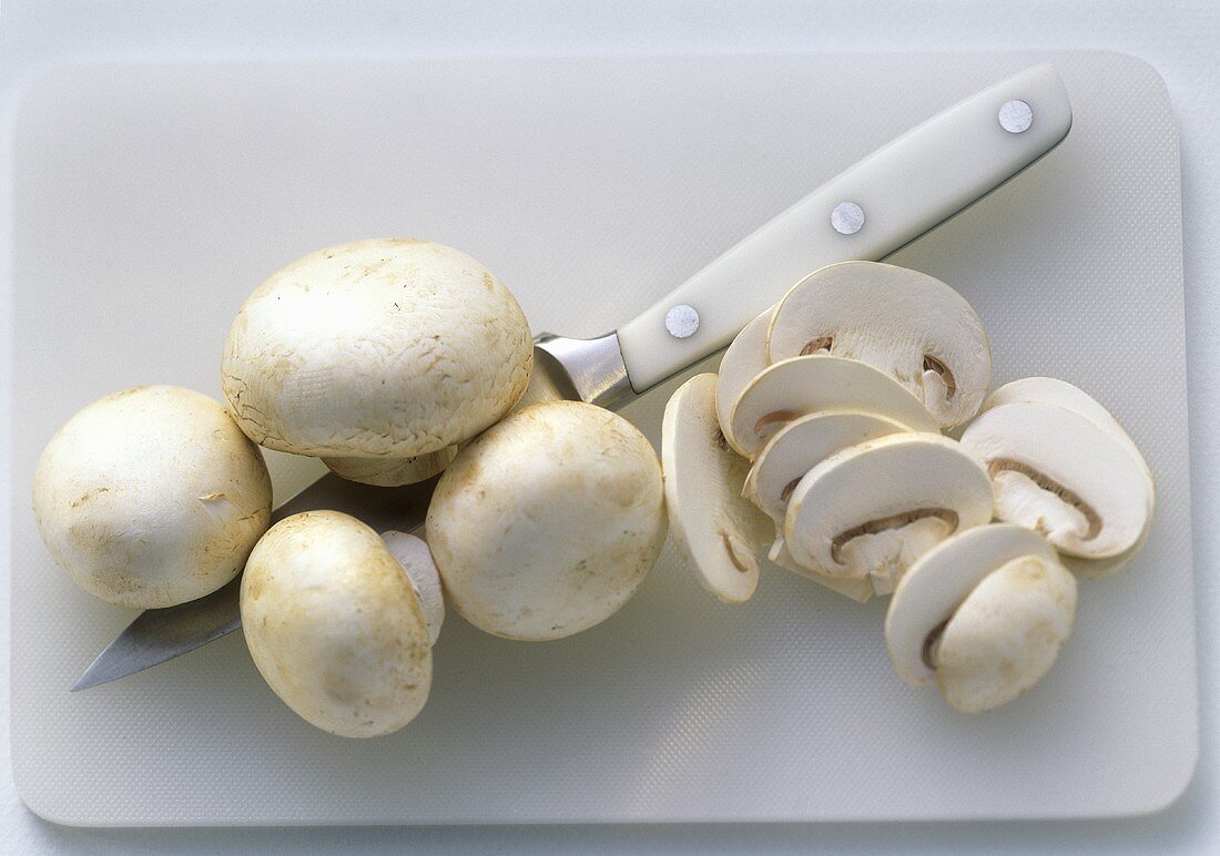 Whole and Sliced White Button Mushrooms on Cutting Board; Knife