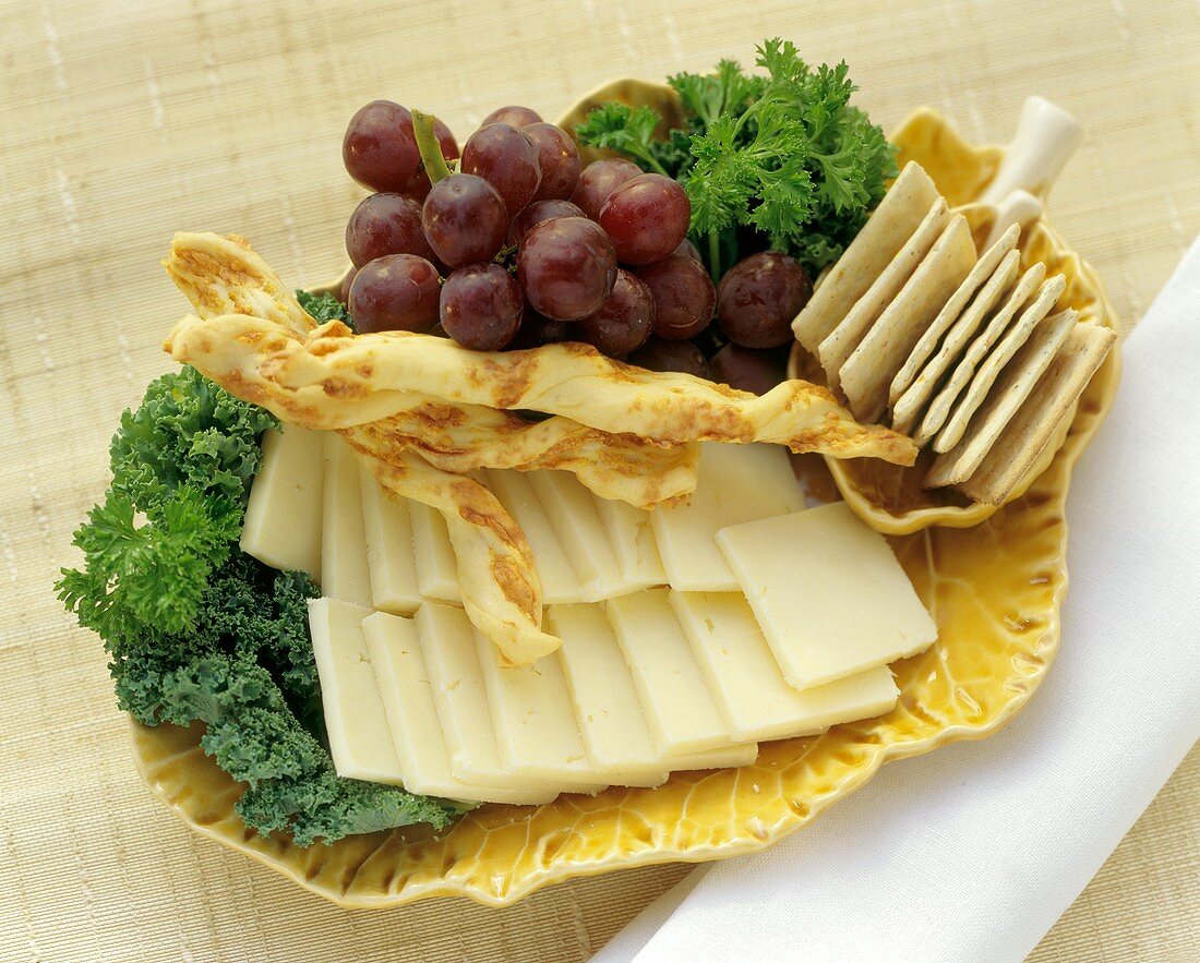 Käsescheiben mit Käsegebäck und Trauben auf einer Platte