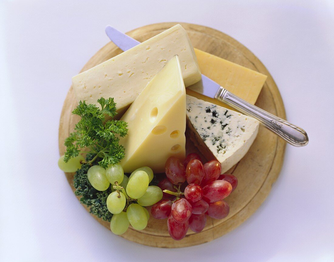 Vier verschiedene Käsesorten mit Trauben auf Holzteller