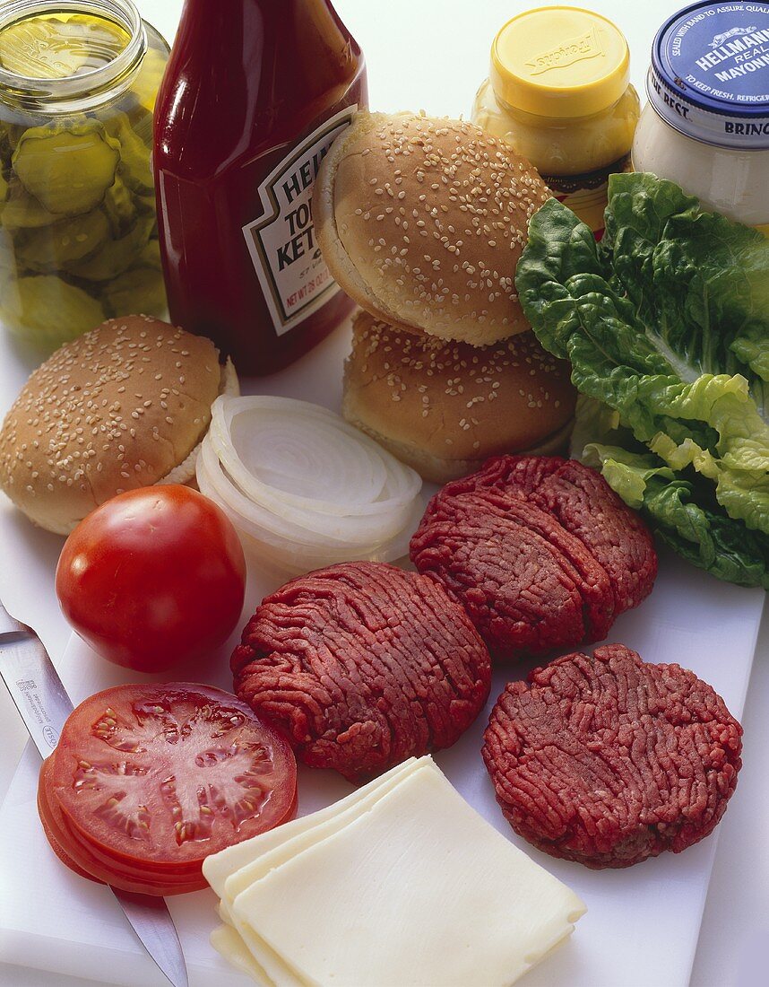 Zutaten für Cheeseburger: Sesambrötchen, rohe Frikadellen etc