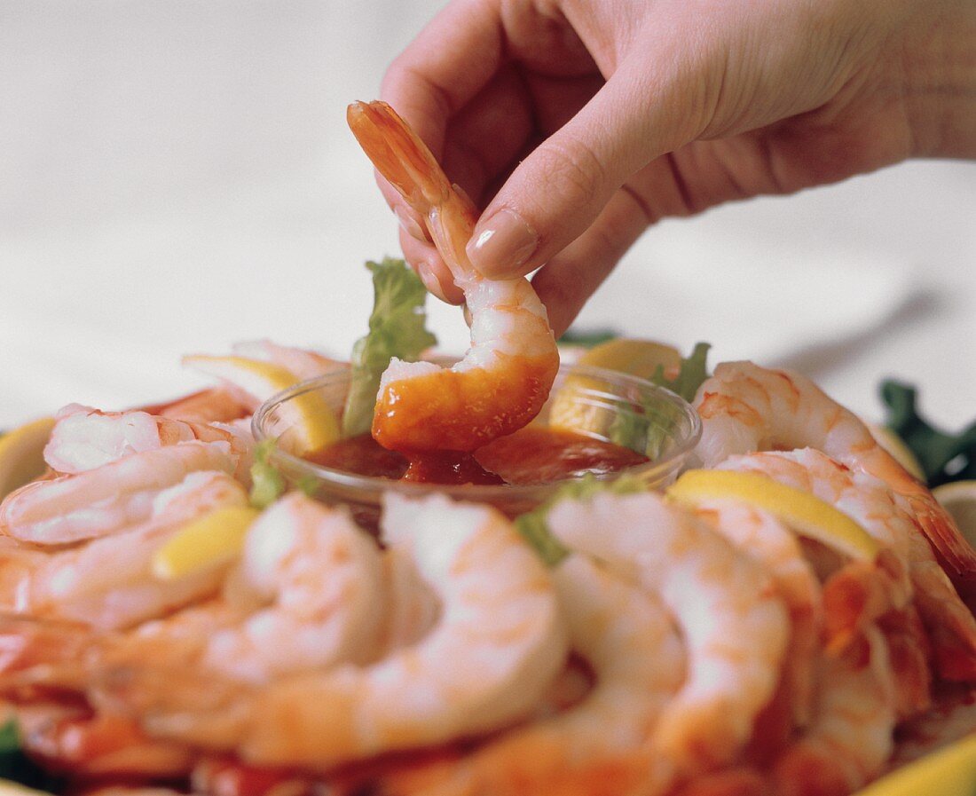 A Hand Dipping a Shrimp into Cocktail Sauce