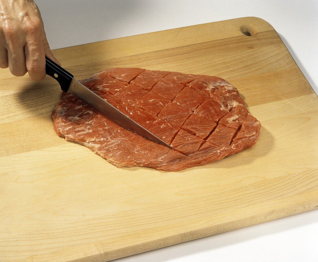 Hand schneidet Quadrate in ein Lendensteak auf Schneidebrett