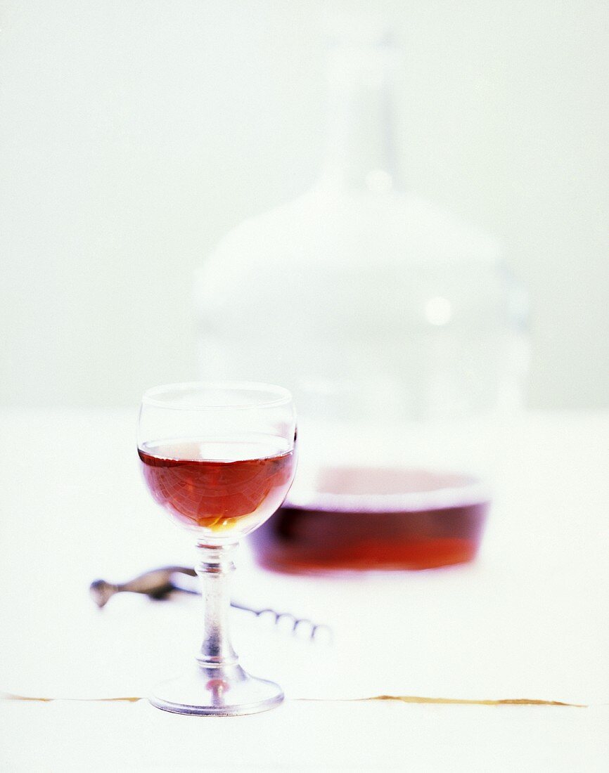Ein Glas Rotwein vor Korkenzieher und Karaffe