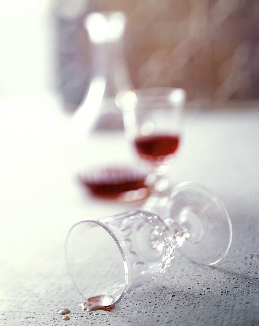 Umgekipptes Glas, dahinter Rotwein im Glas und in Karaffe