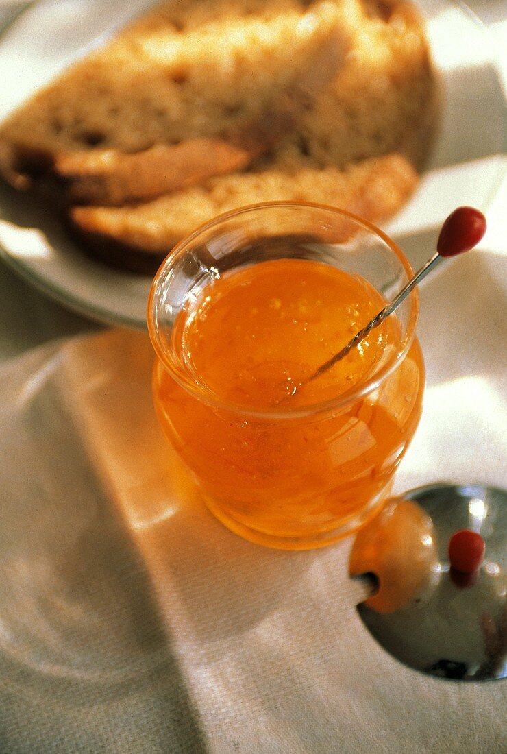 Orangenmarmelade in einem Glasgefäss; Brotscheiben auf Teller