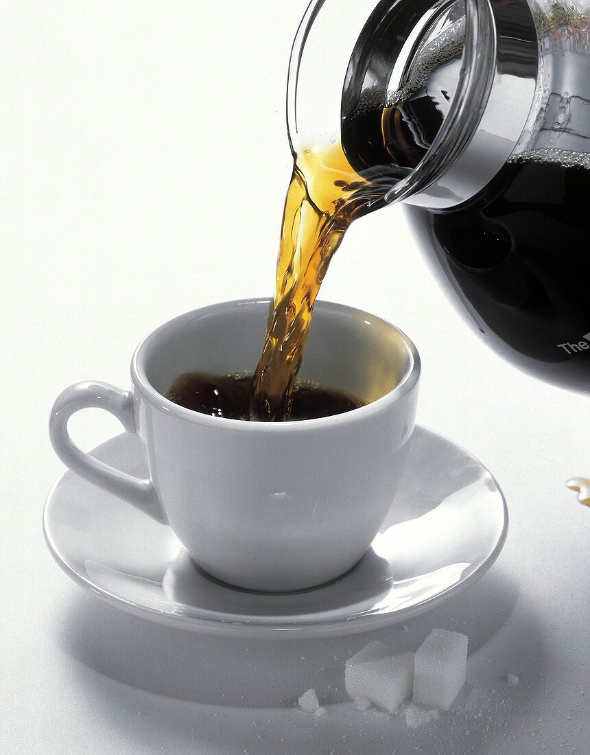 Schwarzer Kaffee wird aus Kanne in eine Tasse gegossen