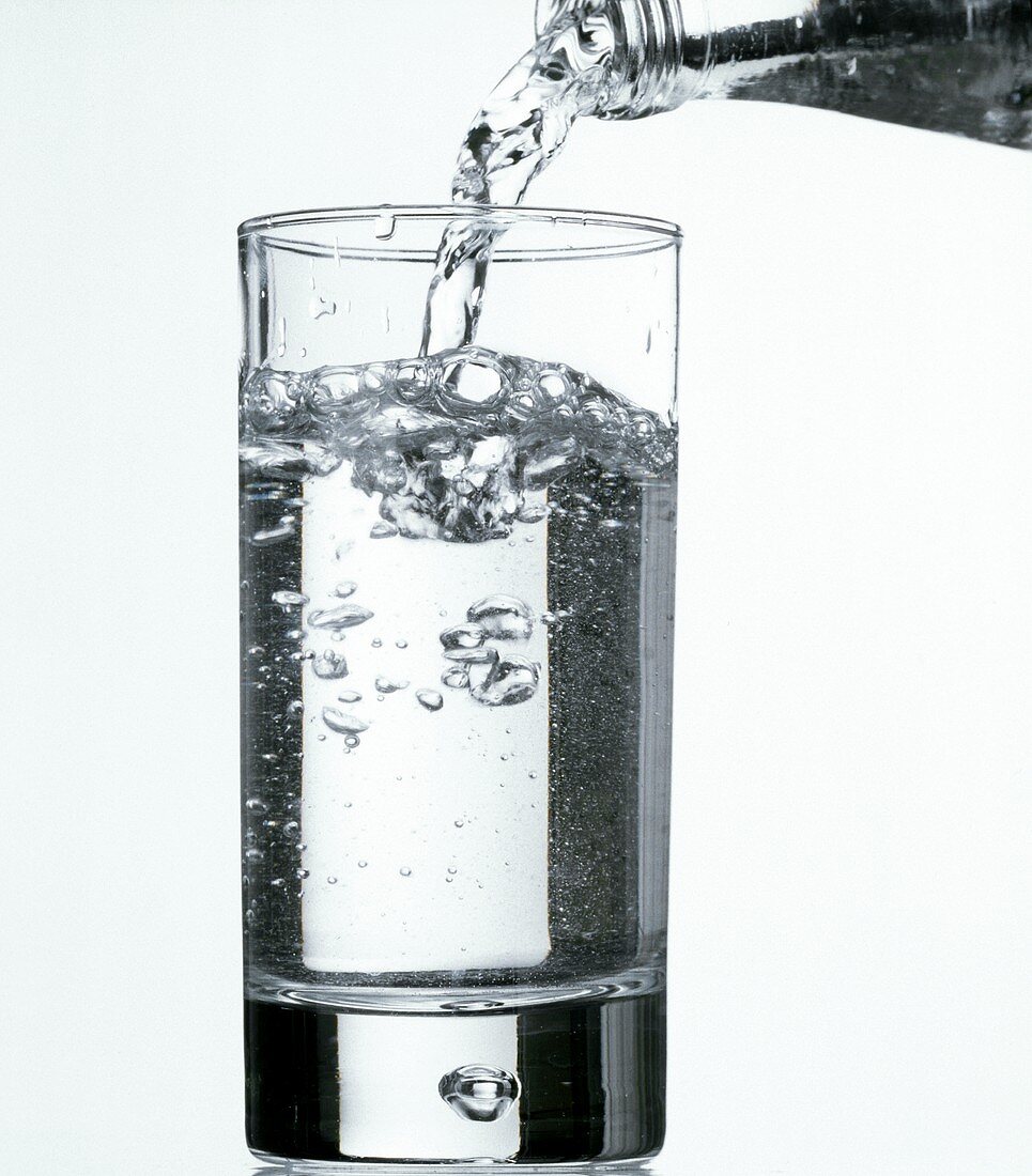 Mineralwasser aus Flasche in Glas gießen