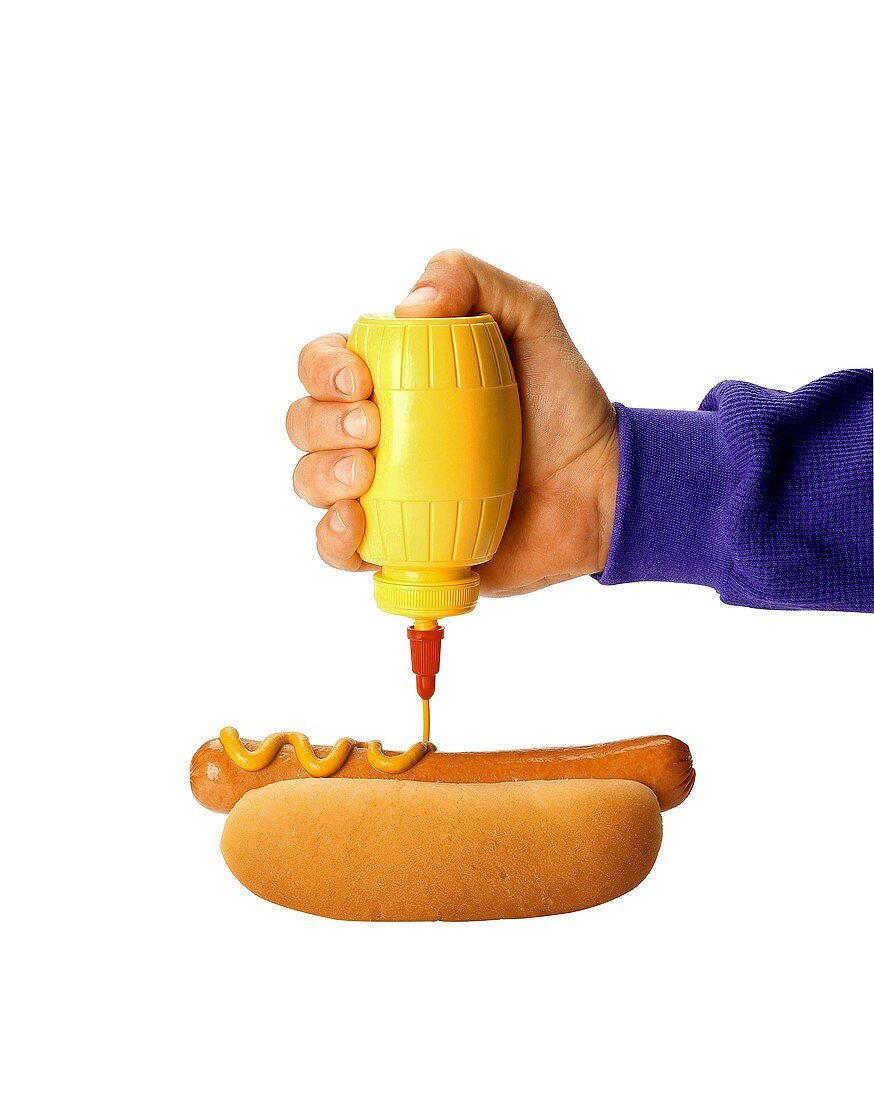 Hand drückt Senf aus Tube auf Hot Dog