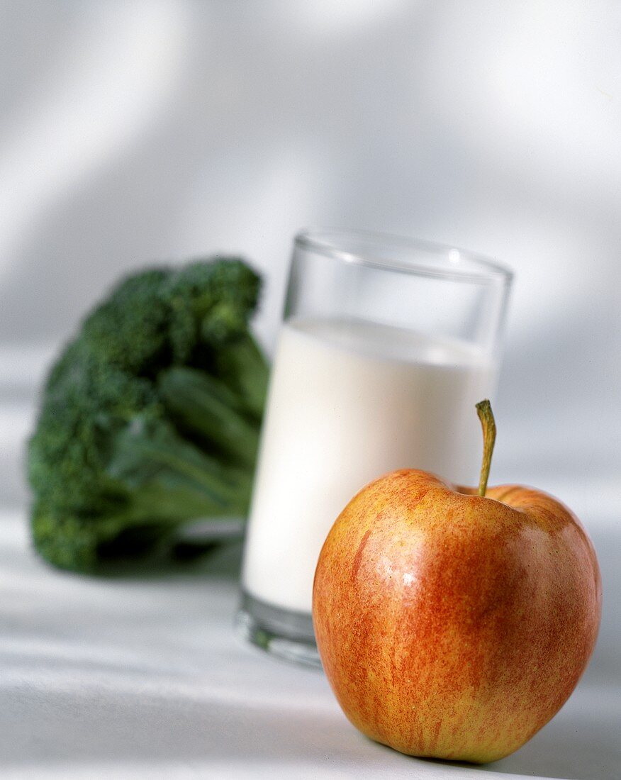 Ein Apfel, dahinter ein Glas Milch und ein Brokkoli