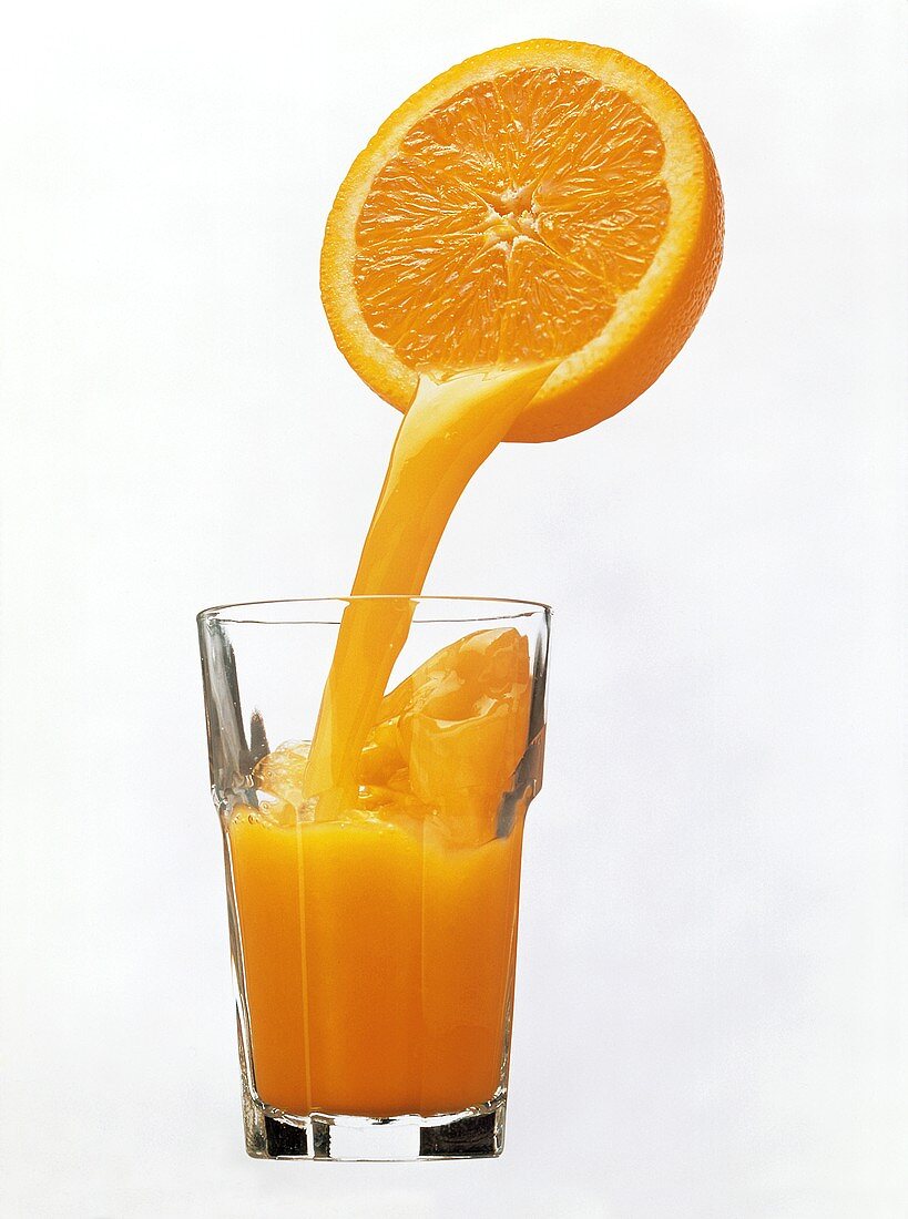 Orangensaft fliesst aus Orangenhälfte in ein Glas