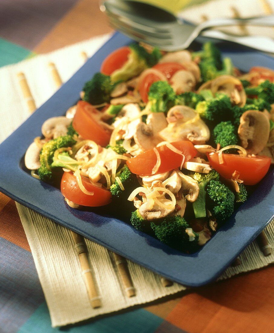 Broccolisalat mit Pilzen und Tomaten auf blauem Teller