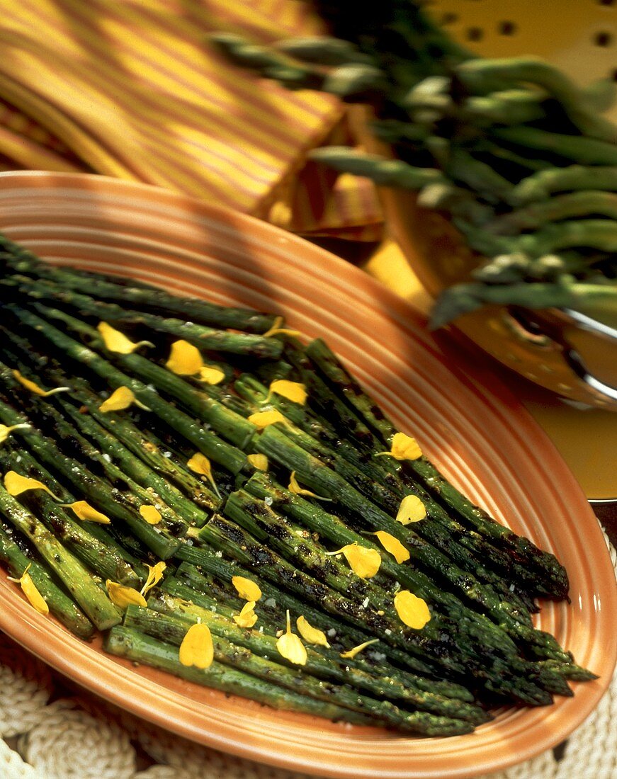 Gegrillter grüner Spargel mit Blütenblättern auf einer Platte