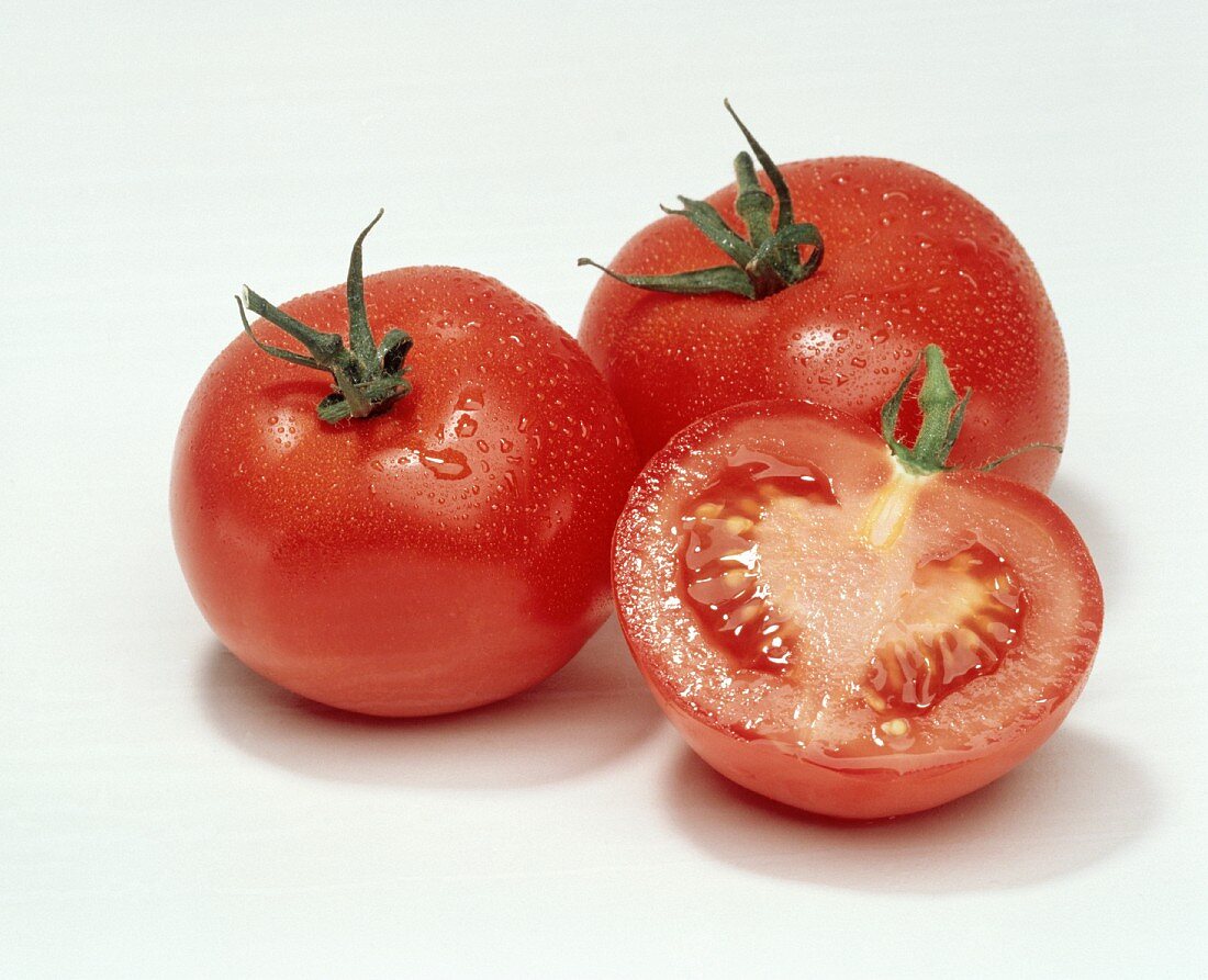 Eine halbe und zwei ganze Tomaten mit Wassertropfen