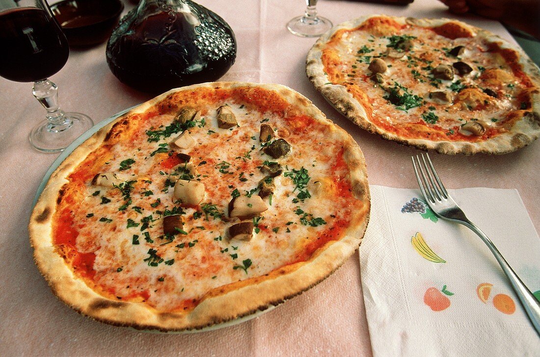 Zwei Pizzen auf Tisch in einem Restaurant; Rotwein