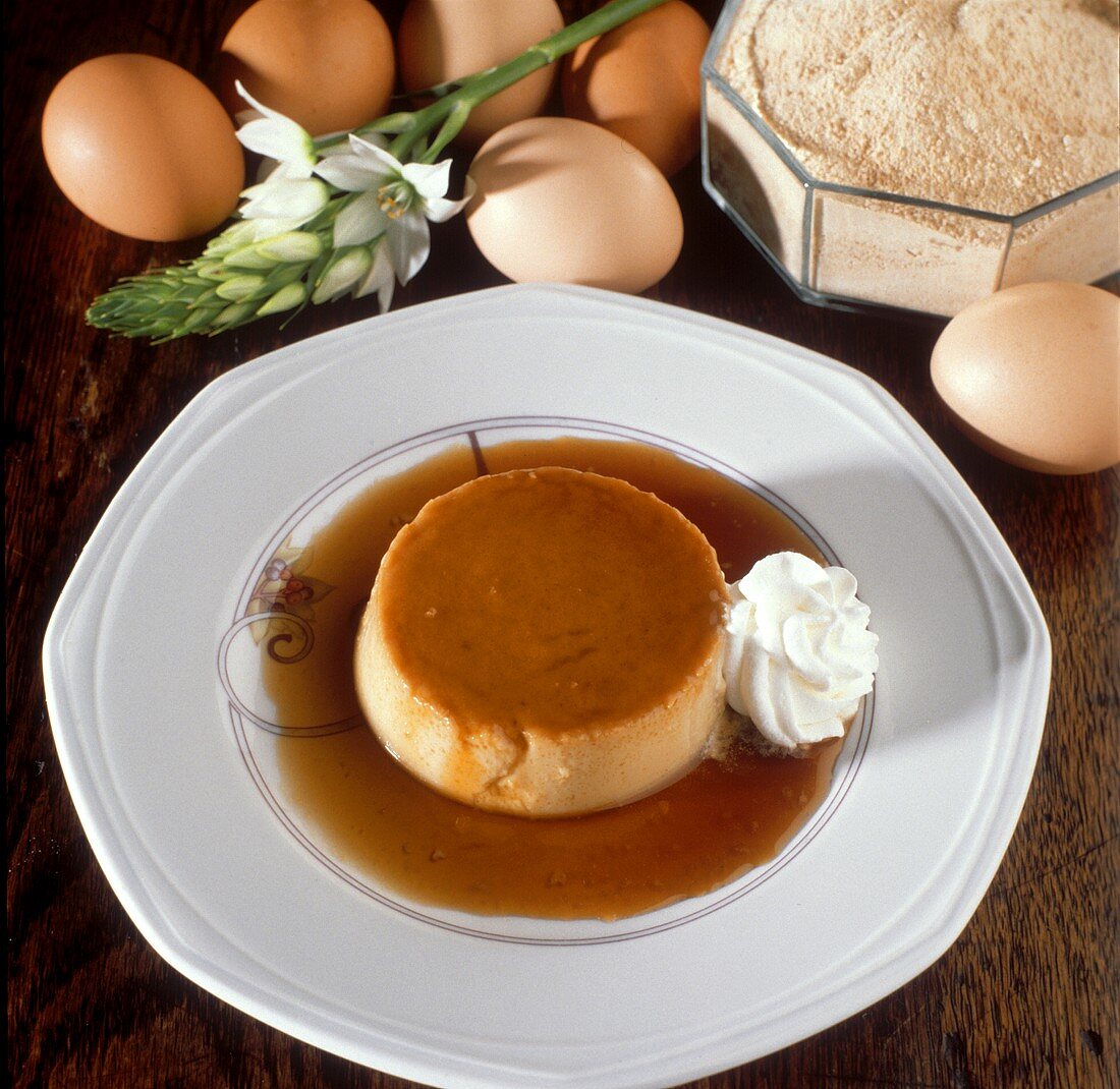 Crème Caramel mit Sahne auf Teller vor Zutaten (Eier, Mehl)