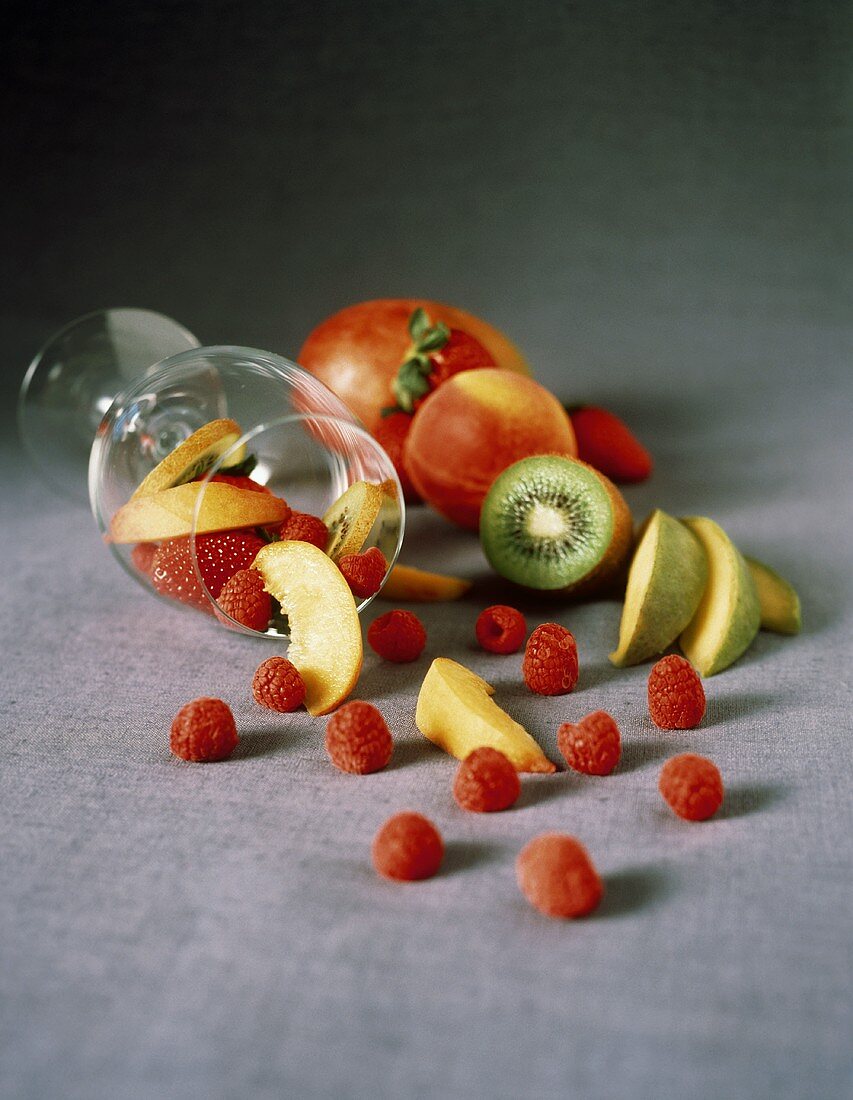 Früchte und Beeren fallen aus einem Glas auf Stoffuntergrund