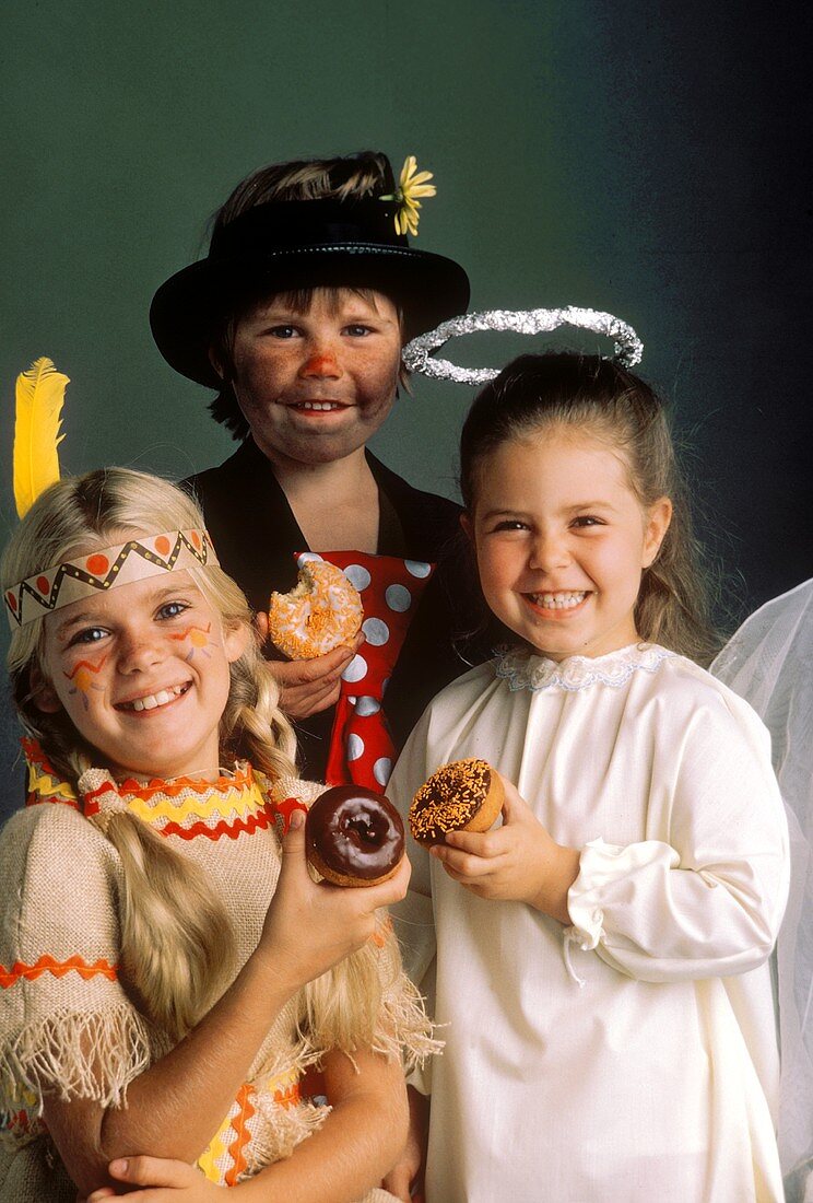 Drei Kinder in Faschings-Kostümen essen Doughnuts