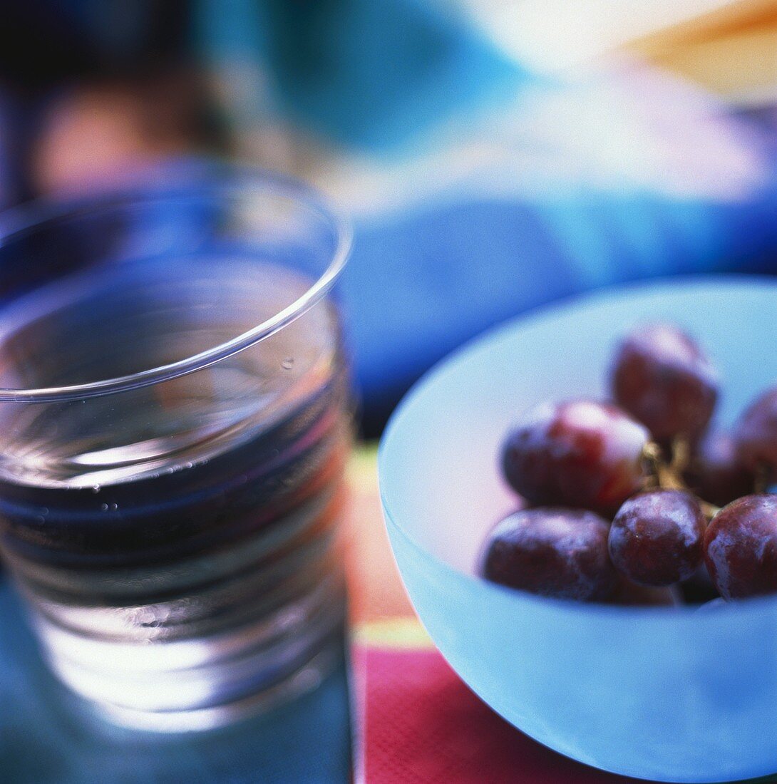 Ein Glas Wasser neben roten Trauben im Schälchen