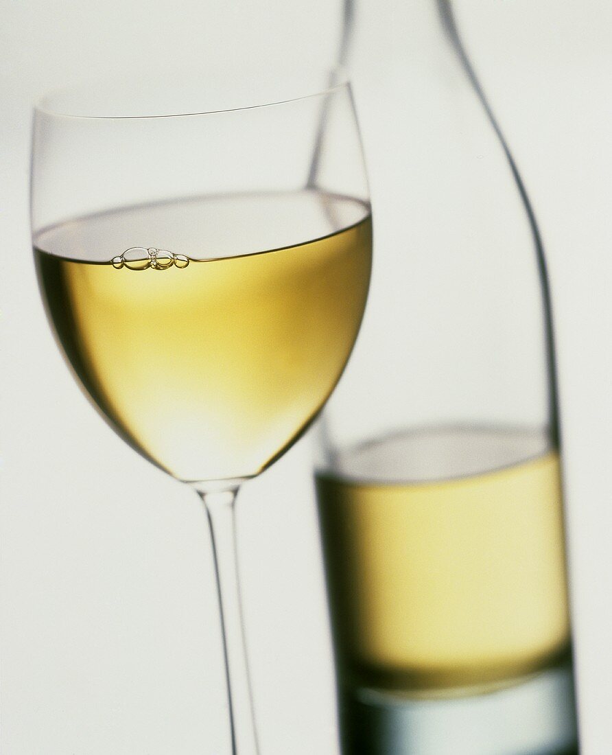Ein Glas Weißwein, dahinter eine Flasche