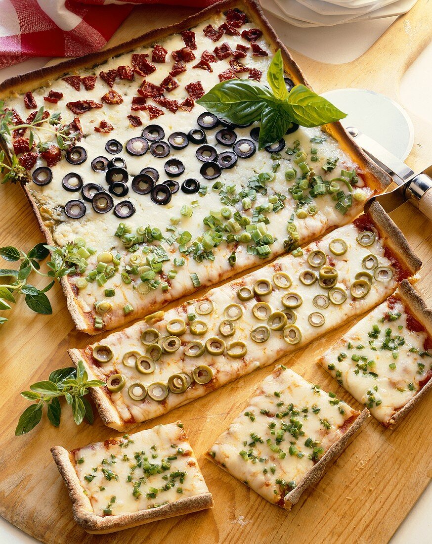 Rectangular Pizza with Rows of Assorted Toppings; Partially Sliced; On Cutting Board