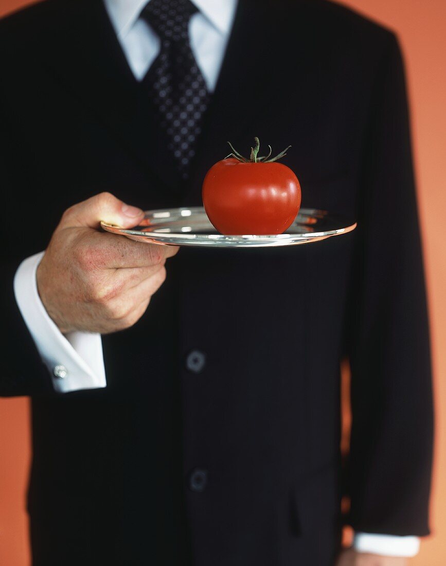 Waiter holding fresh tomato on silver tray