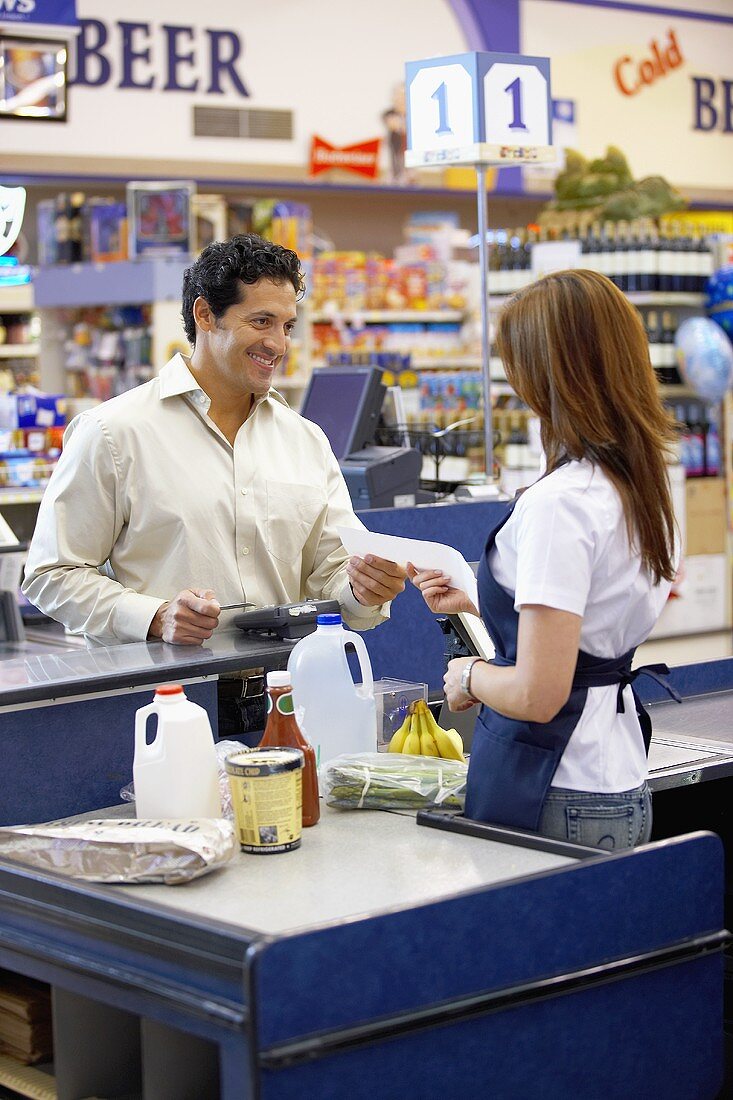 Kassiererin im Supermarkt übergibt Kunden die Rechnung