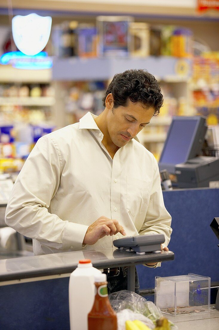 Man Punching Pin Number into Credit Card Machine to Pay for Groceries