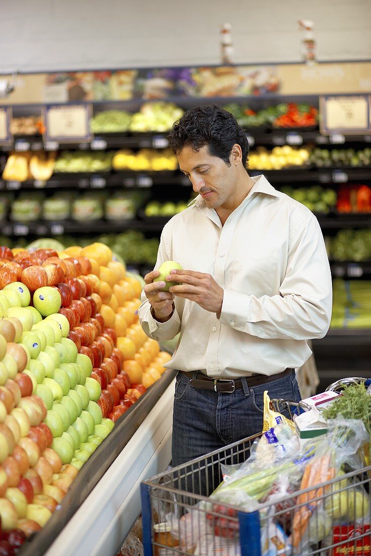 Mann wählt Apfel aus am Obststand im Supermarkt