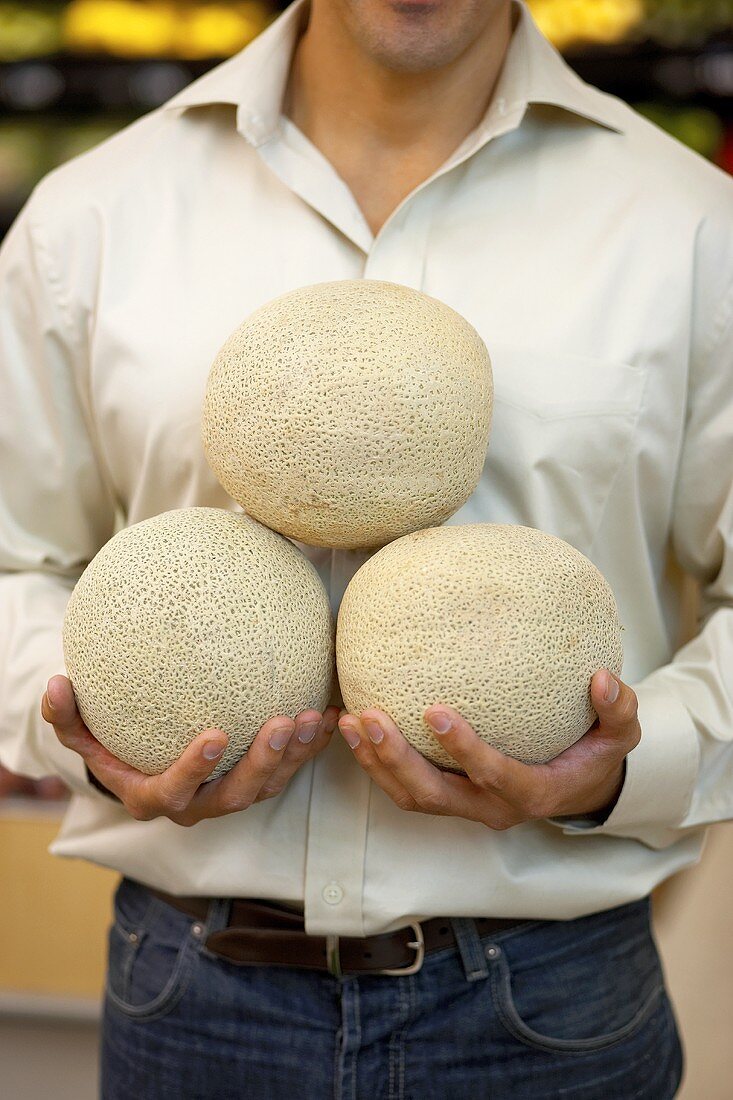 Man holding three melons in supermarket