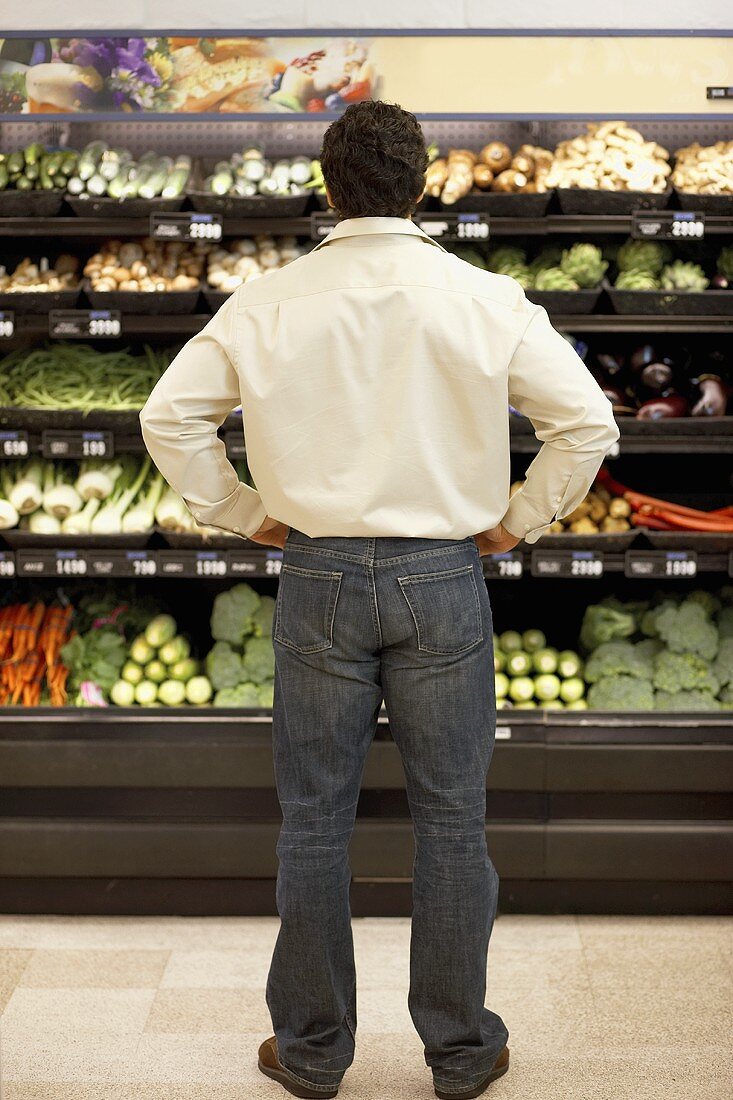 Mann steht nachdenklich in Gemüseabteilung im Supermarkt