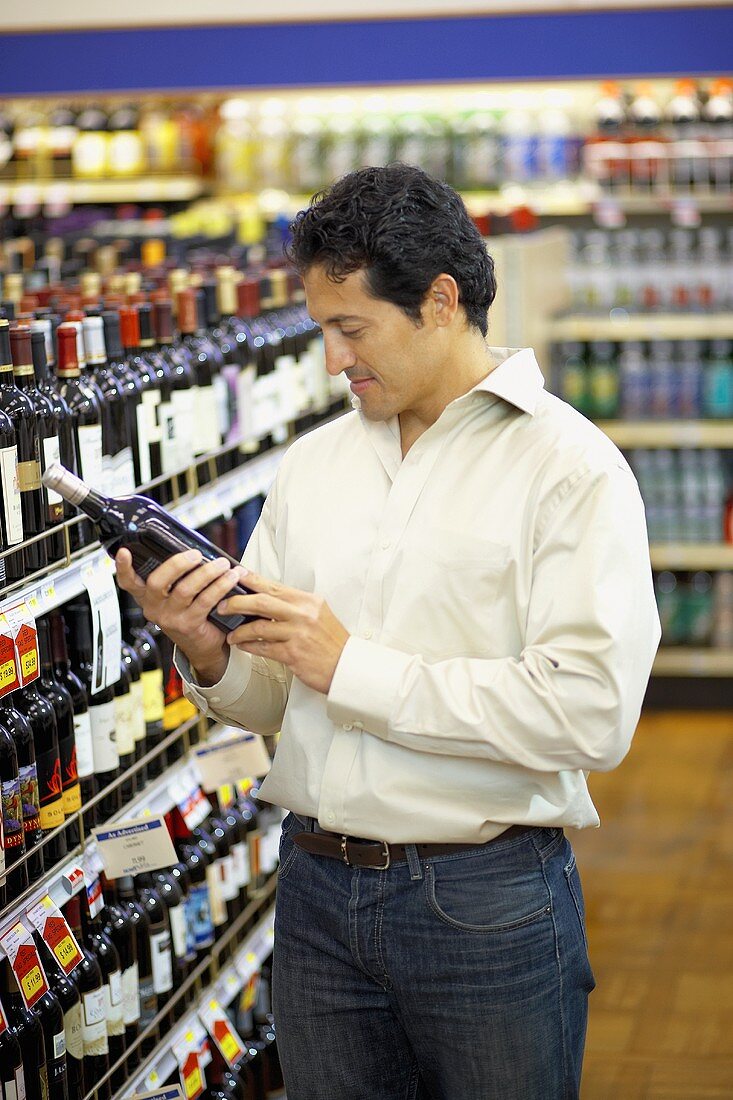 Mann liest Etikett einer Weinflasche im Supermarkt