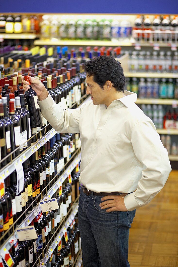 Mann nimmt Weinflasche aus Regal im Supermarkt