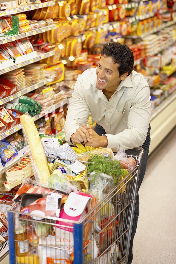 Lächelnder Mann mit vollem Einkaufswagen im Supermarkt