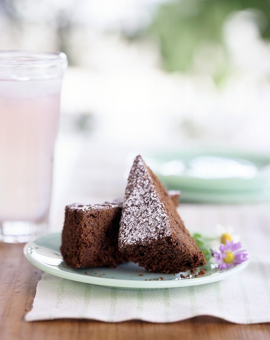 Two Brownie Wedges Topped with Powdered Sugar on a Plate with a Glass of Milk