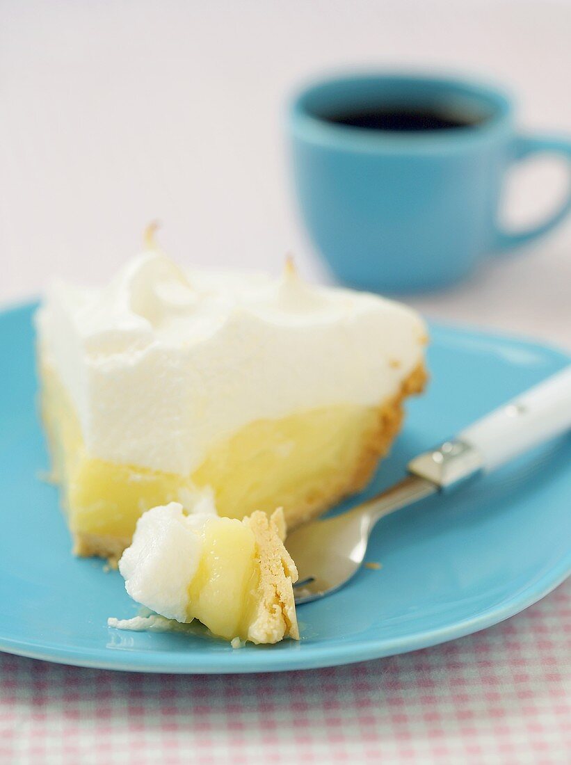 Piece of lemon meringue pie in front of blue coffee cup (USA)