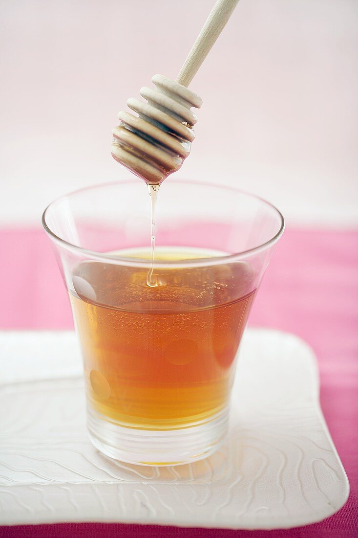 Honey trickling from honey dipper into glass