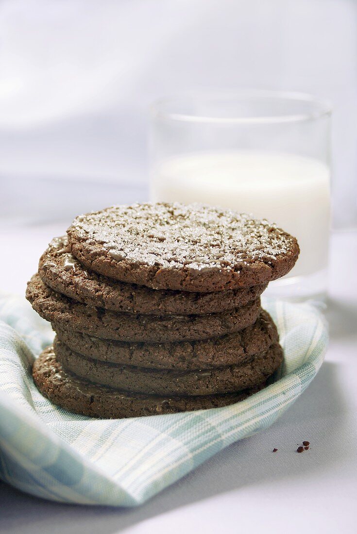 A pile of chocolate biscuits in front of a glass of milk