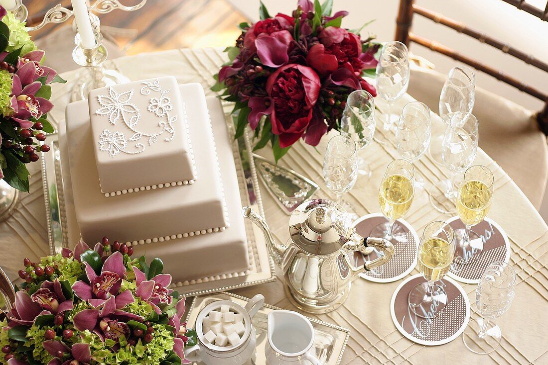 Three-tiered white wedding cake, flowers & champagne glasses