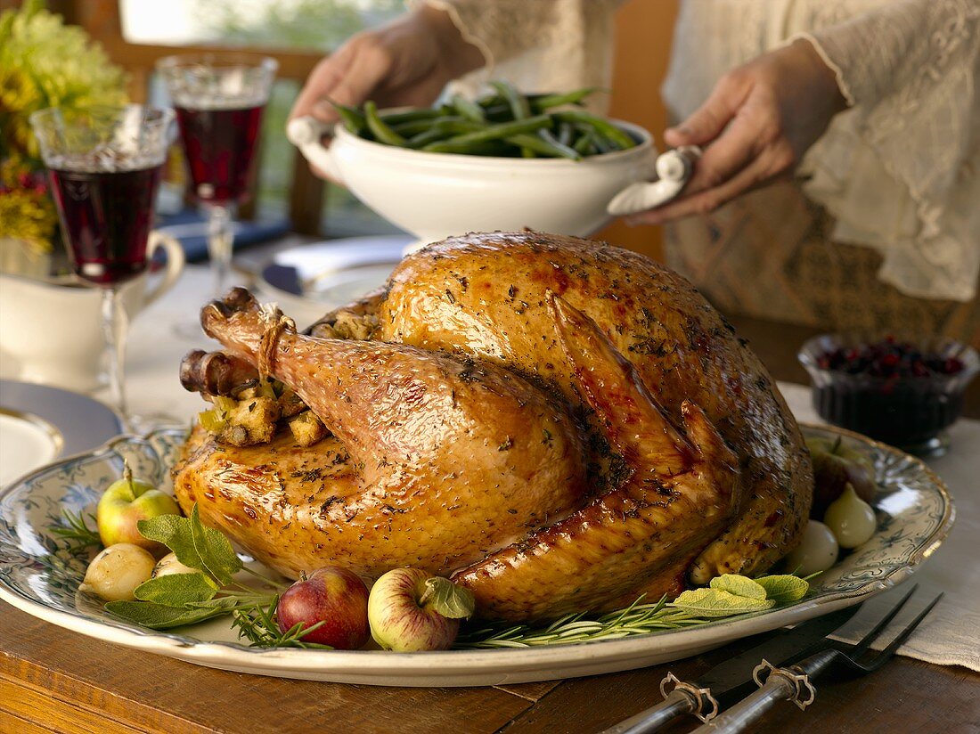 Stuffed turkey on table, woman serving green beans (USA)