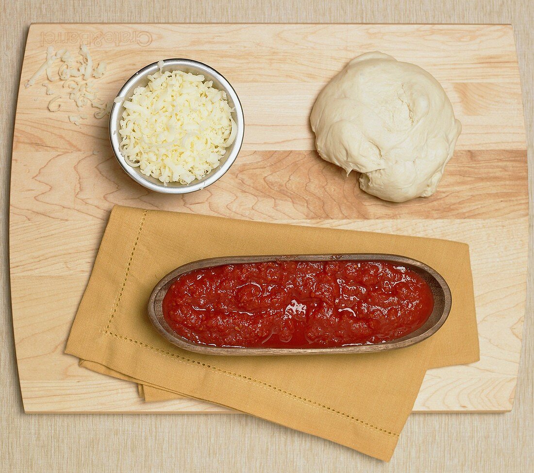 Pizza ingredients on board (dough, tomato sauce, cheese)