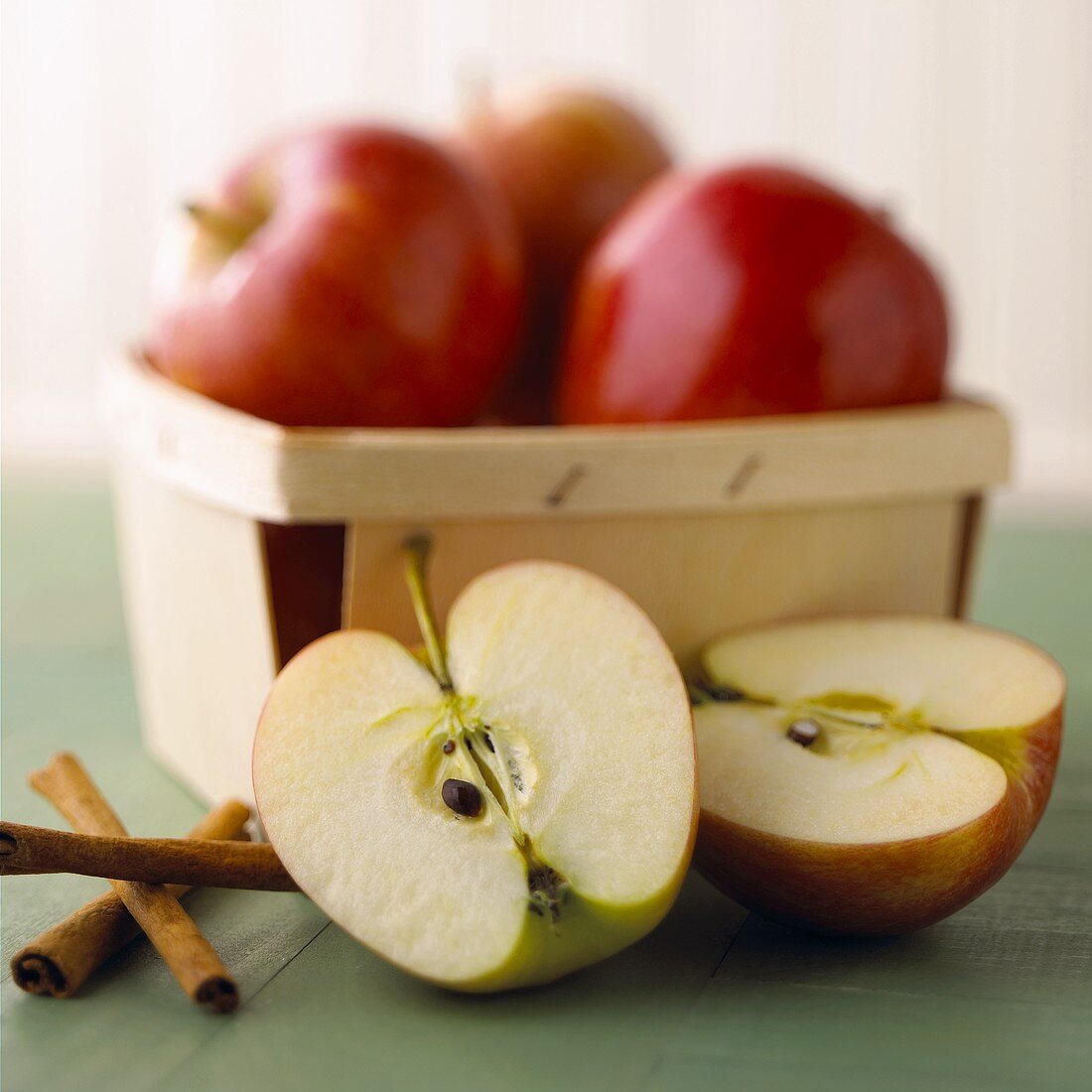 Äpfel im Spankorb, davor zwei Apfelhälften und Zimtstangen