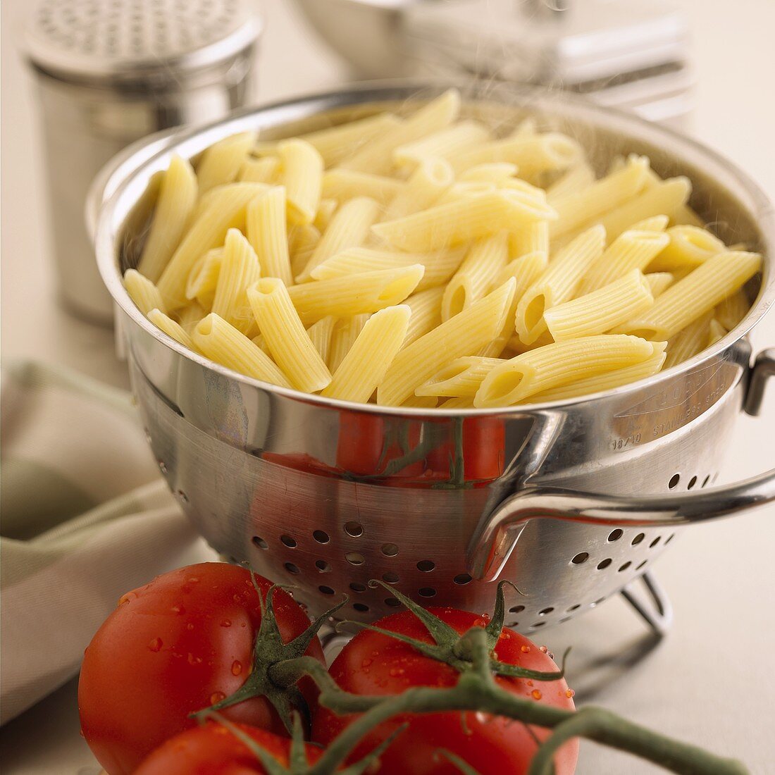 Cooked penne in strainer (steaming), fresh tomatoes beside it