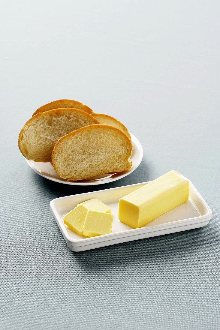Stück Butter in weisser Butterdose, Brotscheiben auf Teller