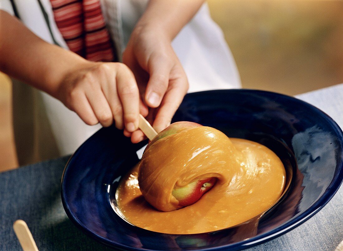 A child's hands rolling an apple in caramel sauce