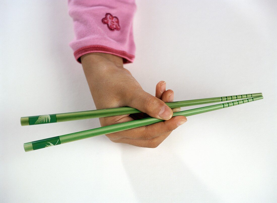 Childs Hand Holding Two Green Chopsticks