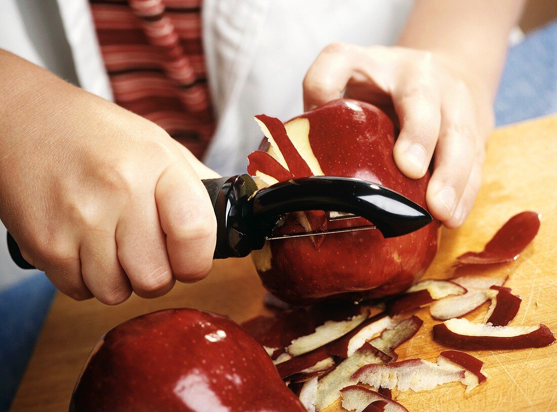 Childs Hands Peeling Red Delicious Apples with a Peeler on a Cutting Board