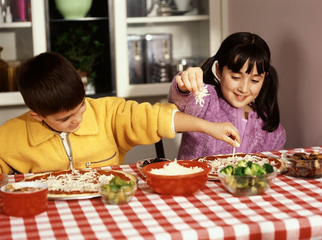Boy and Girl Sitting at a Table Making Individual Pizzas, Toppings, Cheese and Broccoli