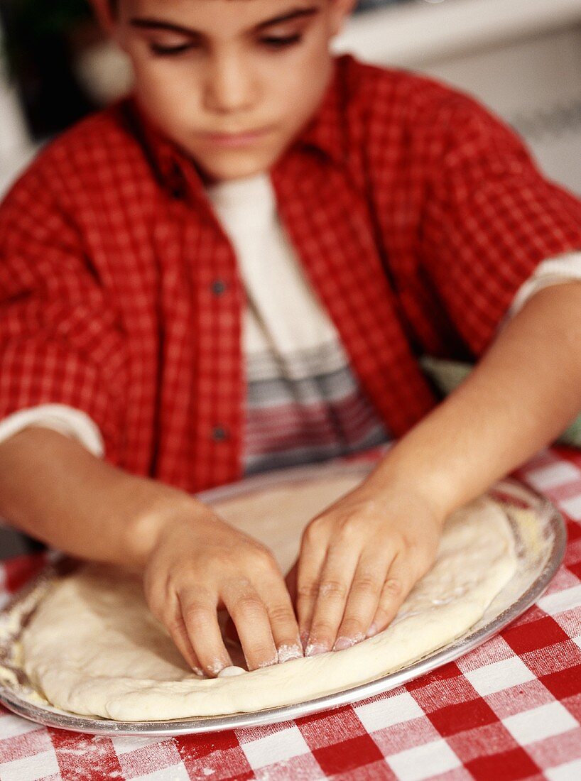 Kleiner Junge formt Pizzateig mit den Händen in Pizzapfanne