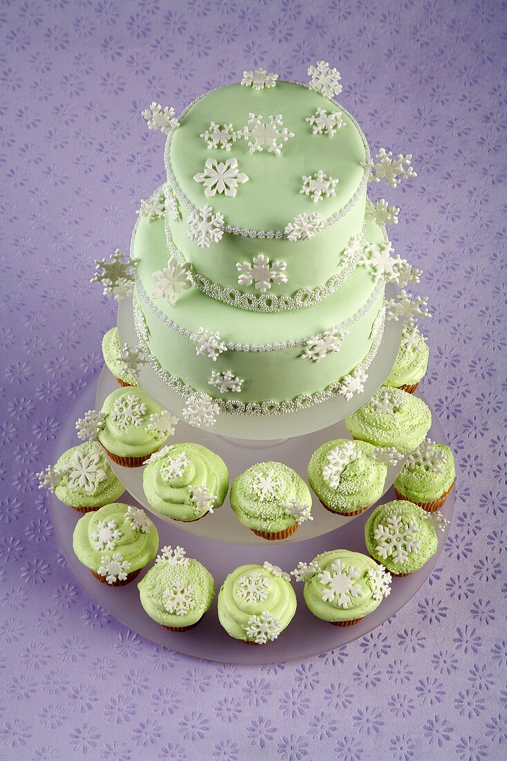 Two Tier Cake with Green Frosting and Snowflake Decorations on Two Tiers of Snowflake Cupcakes